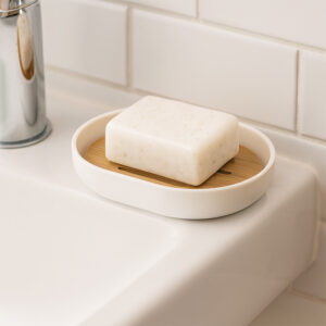 White soap dish with bamboo insert holding square soap bar on sink edge