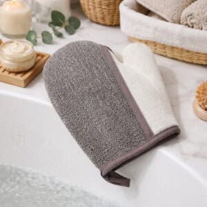 Gray and white dual-texture exfoliating glove on spa table with towels and skincare products
