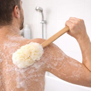 Man using a long-handled mesh loofah bath brush to scrub his soapy back in the shower.