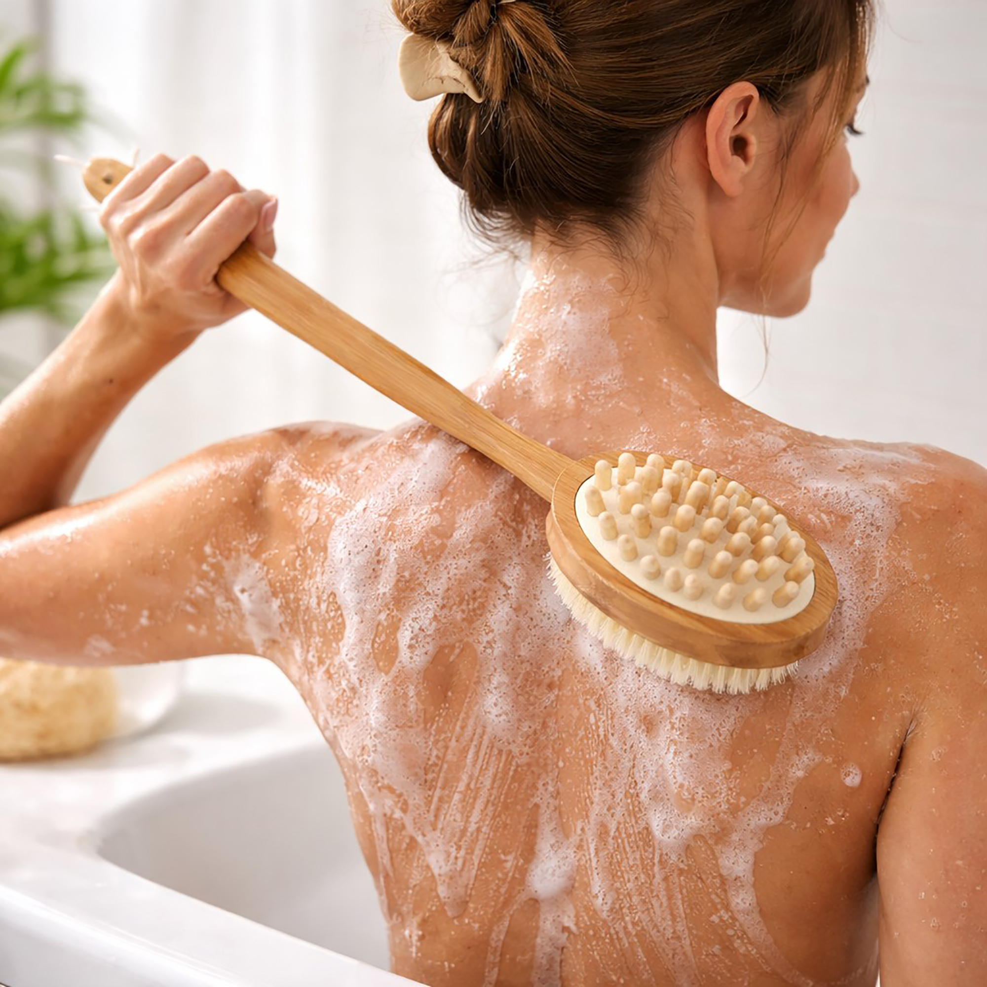 Woman using the dual-sided wooden body brush to scrub her soapy back while bathing, with the massage nodule side facing out.