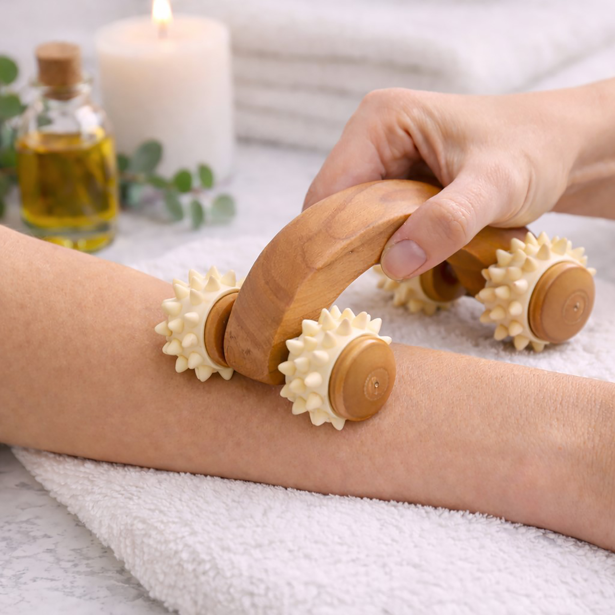 Hand using a wooden handheld massager with four spiked rollers on a person's leg during a spa treatment.