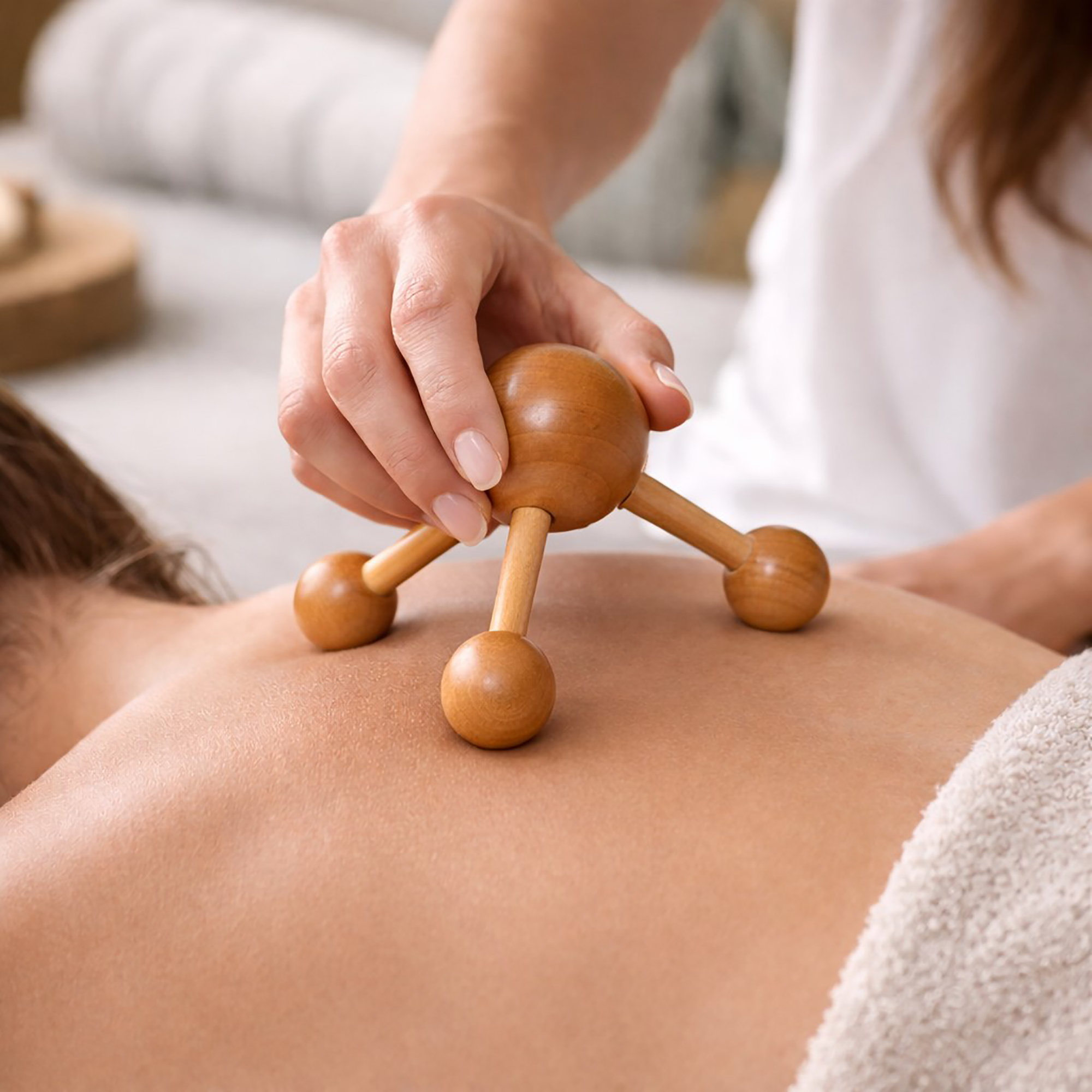 Hand using a wooden node massager on a person's back during a spa treatment.