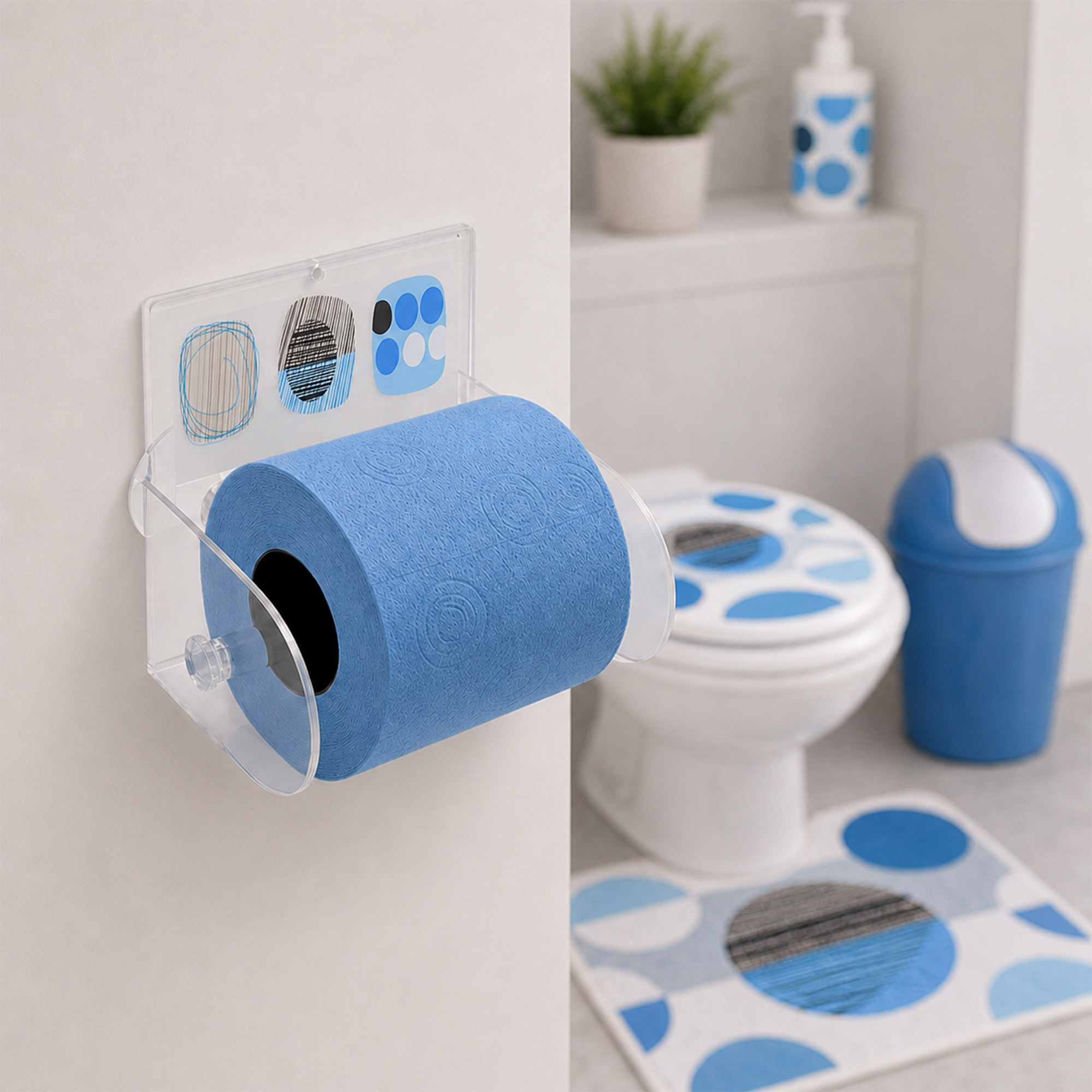 Street Art clear acrylic toilet paper holder mounted on wall holding a blue roll, with toilet, matching blue-and-grey seat cover, blue swing-lid bin, and coordinating bath mat in the background.