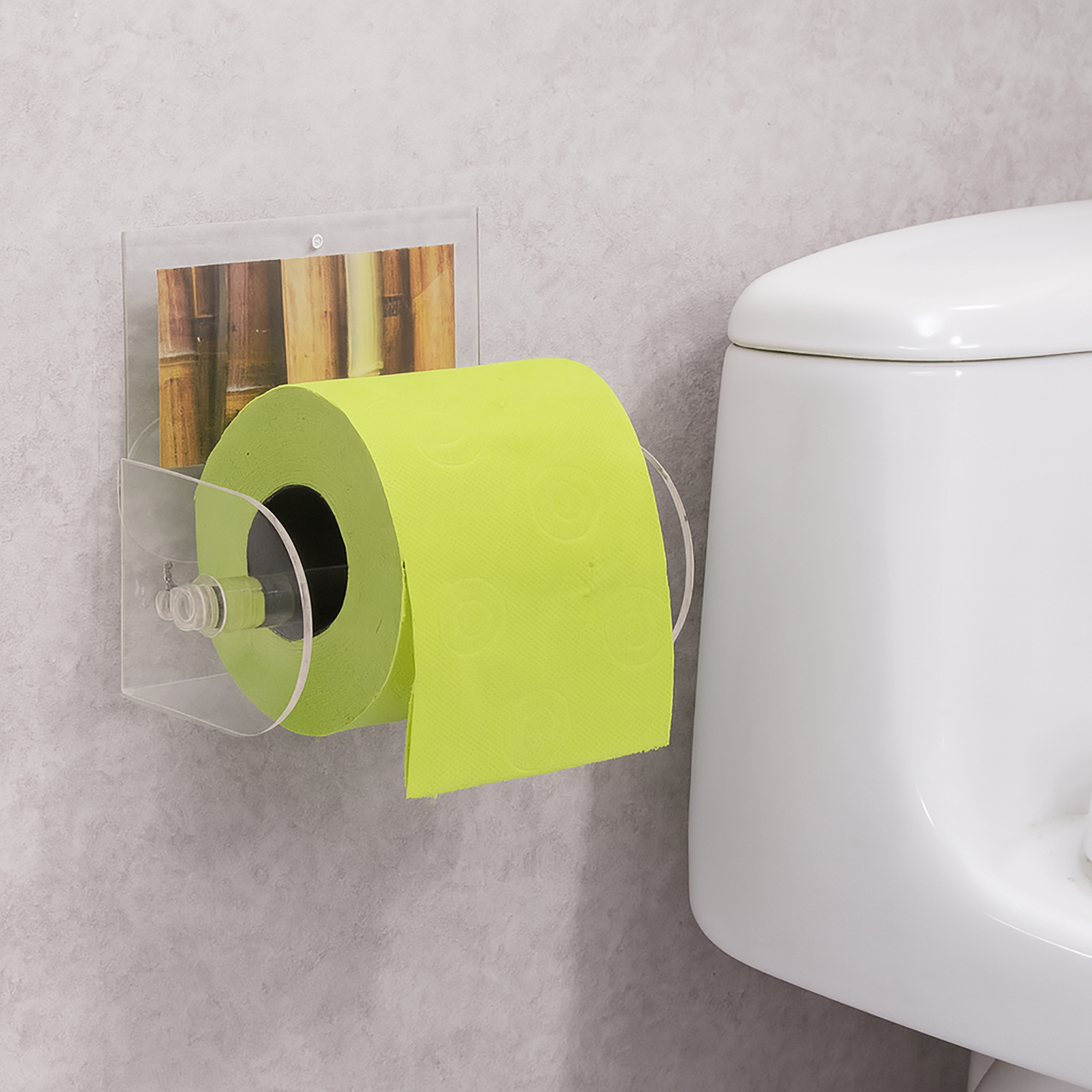 Bamboo clear acrylic toilet paper holder suction-mounted on grey wall beside a toilet, holding a lime-green roll. Graphic insert shows a bamboo-stalk photo.