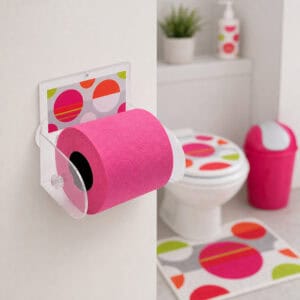 Eclats clear acrylic toilet paper holder mounted on wall holding a hot pink roll, with toilet, matching polka-dot seat cover, pink swing-lid bin, and coordinating bath mat in the background.