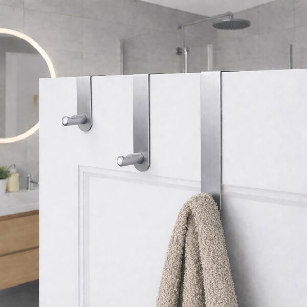 "Three brushed steel over-door hooks on white paneled bathroom door with beige towel on lowest hook"
