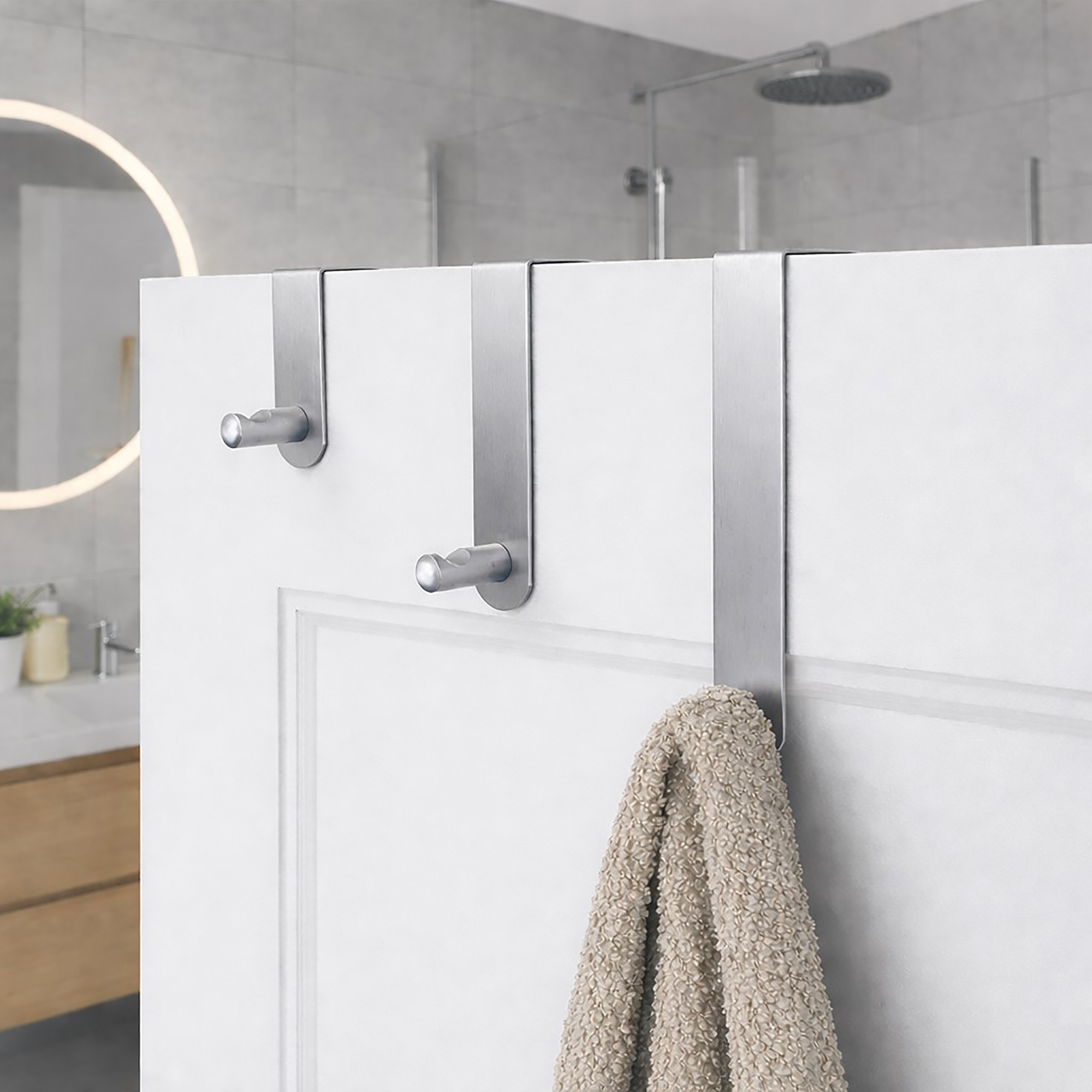 "Three brushed steel over-door hooks on white paneled bathroom door with beige towel on lowest hook"
