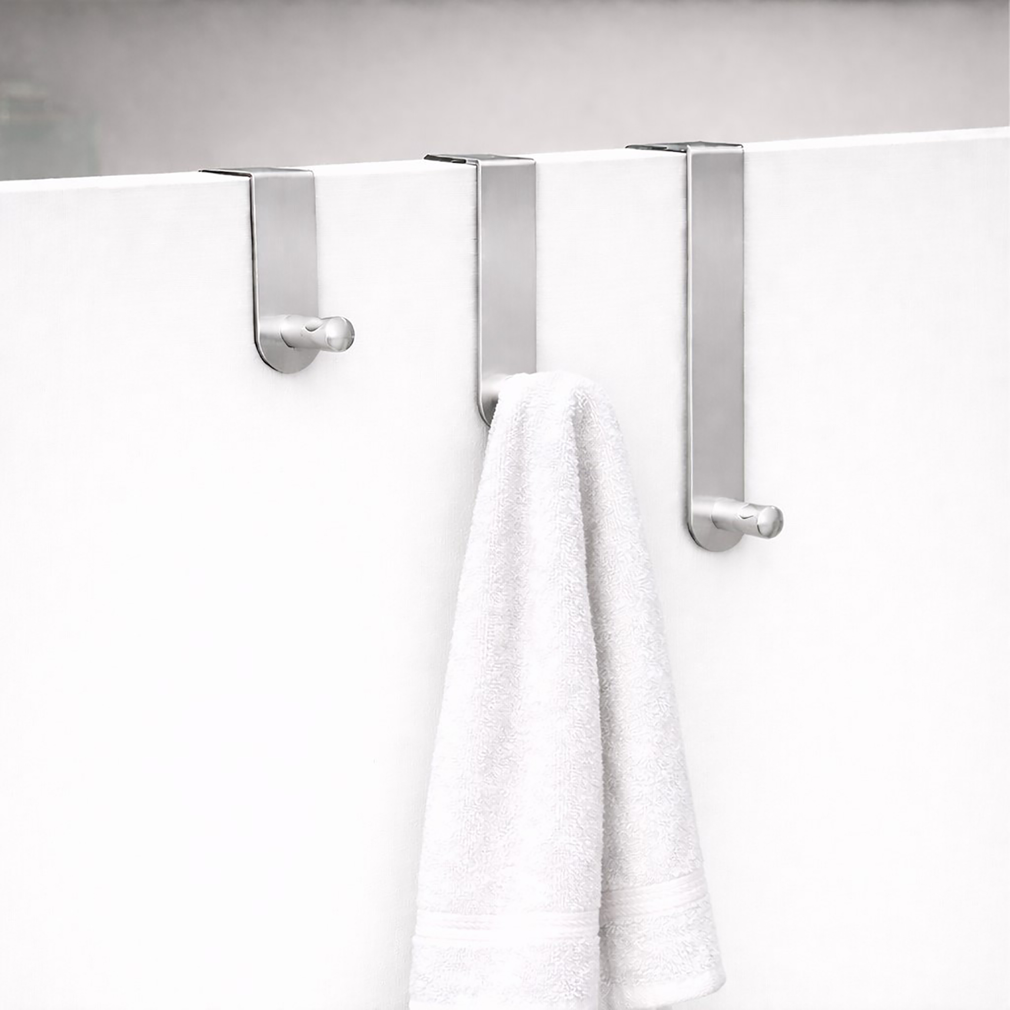 "Three brushed steel over-door hooks on white door with white bath towel draped over middle hook"