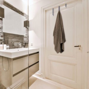 "Brushed steel over-door hook holding brown bath towel on cream paneled bathroom door"