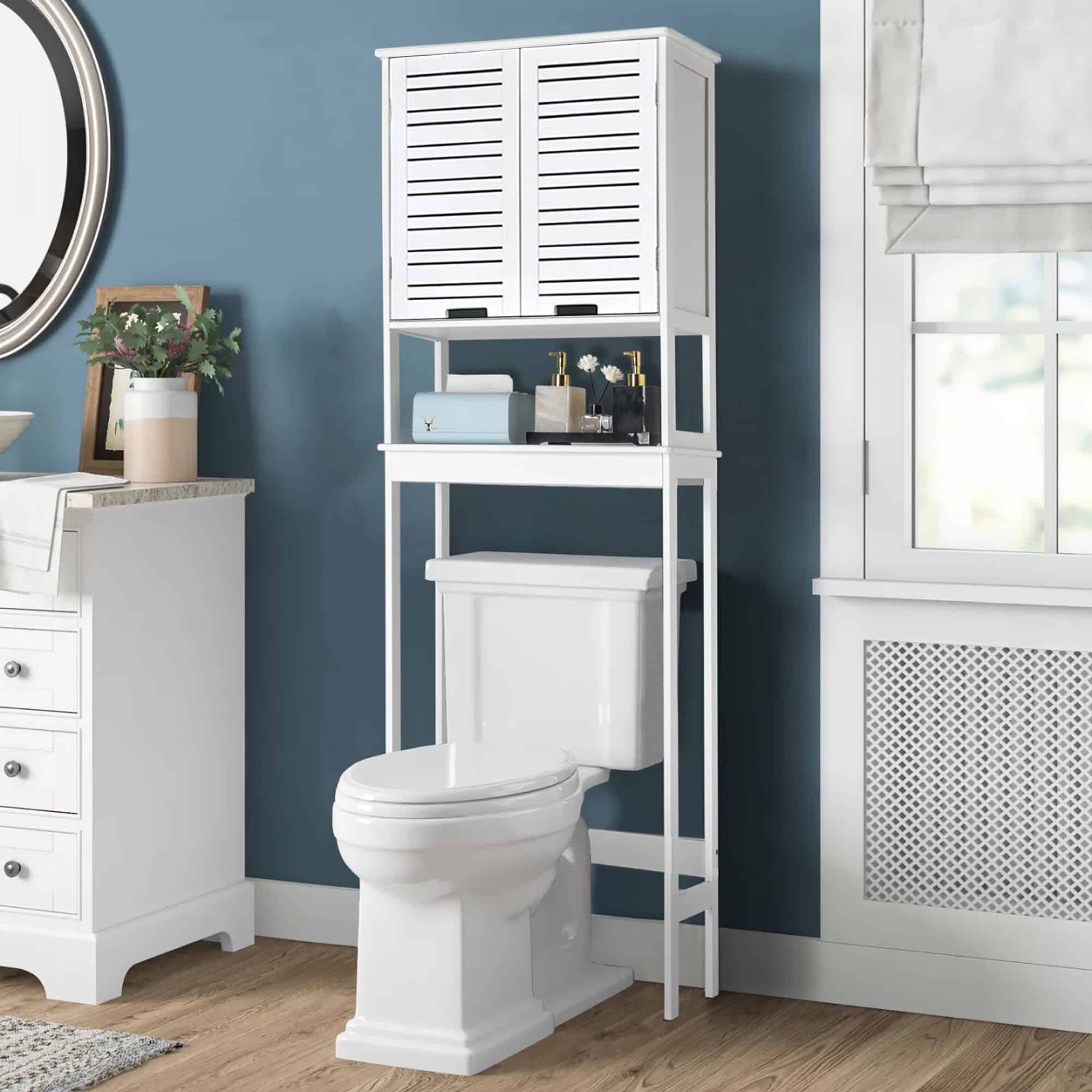 In-use view of over-the-toilet cabinet in bathroom – White over-the-toilet storage cabinet in a modern bathroom with a blue wall, accessorized with decorative and functional items.