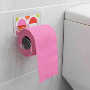 Eclats clear acrylic toilet paper holder suction-mounted on grey tile beside a toilet tank, holding a pink roll with paper hanging down.