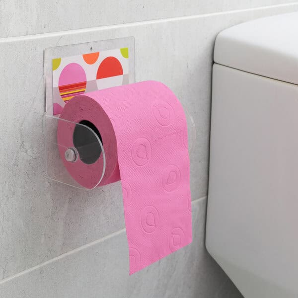 Eclats clear acrylic toilet paper holder suction-mounted on grey tile beside a toilet tank, holding a pink roll with paper hanging down.