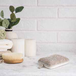Spa bathroom scene with exfoliating pad, plant, towels, and skincare products on marble surface