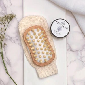 Spa scene with massage brush, conditioning cream jar, towels, and plant on marble surface