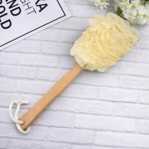 Body brush with loofah on marble surface next to flowers and card