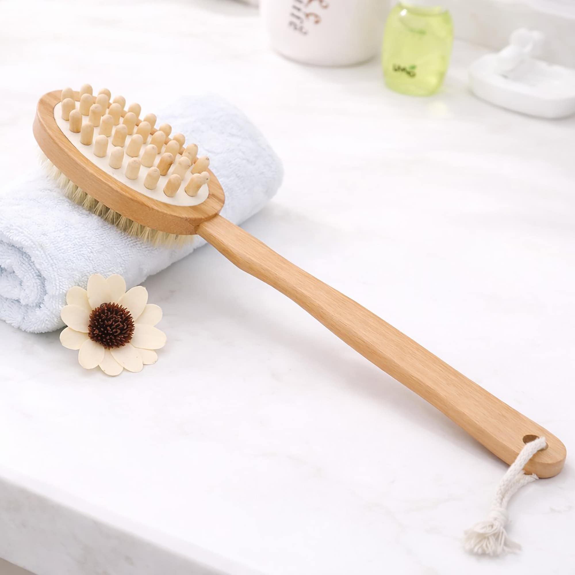 Dual-sided body brush styled with white towels, decorative flower, and bathroom accessories