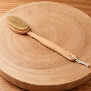 Long-handled wooden bath brush with natural bristles displayed on a round wood slice surface.