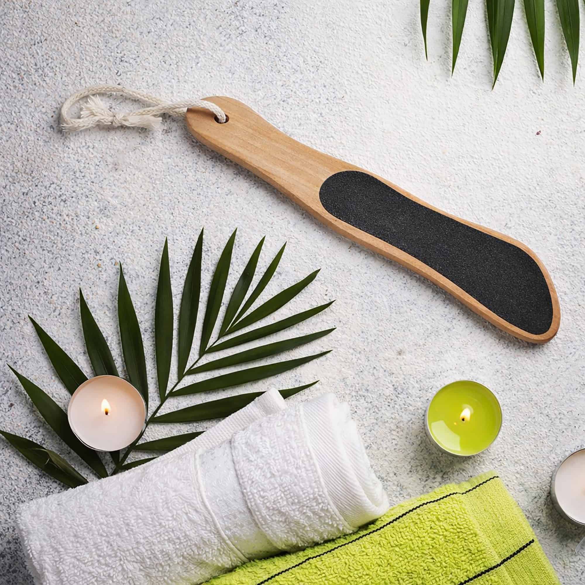 Wooden foot file styled on marble surface with spa accessories including palm leaves, candles, and green towels