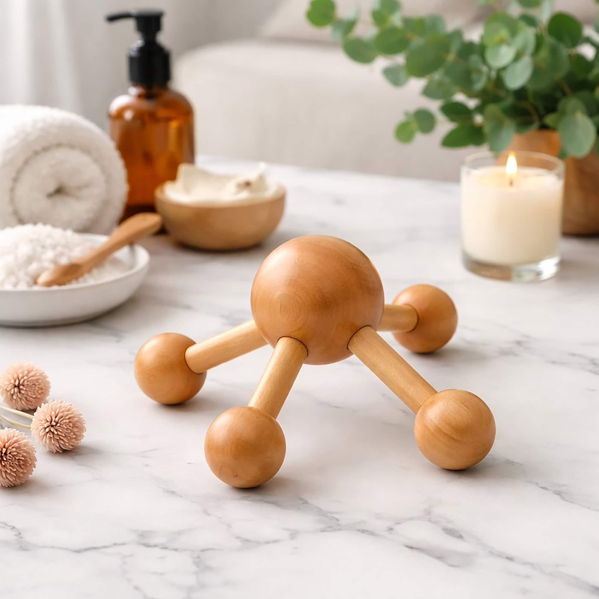 Wooden node massager on a marble surface surrounded by a candle, towel, lotion, bath salts, and eucalyptus.