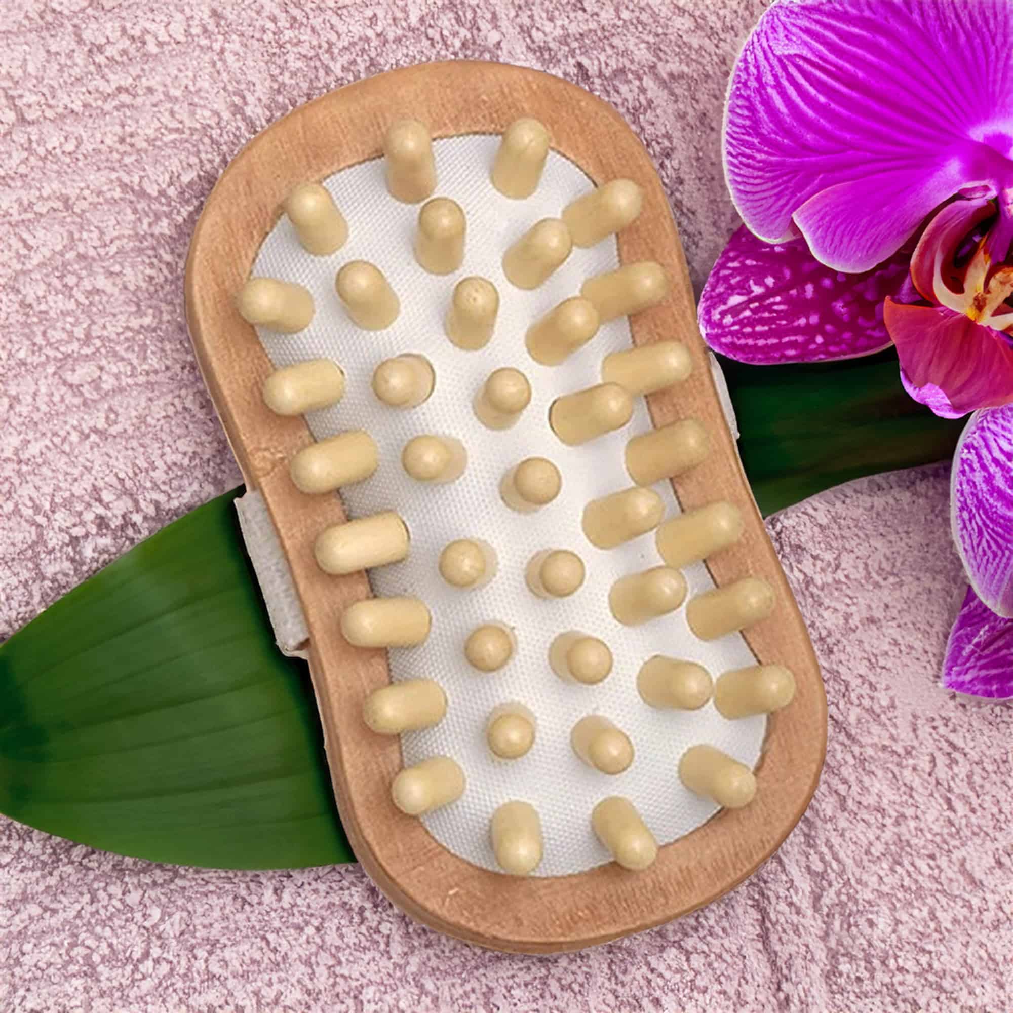 Body Care Massage Brush Well-Being Natural Wood handheld massager with rounded pegs on a soft towel, next to a purple orchid flower.