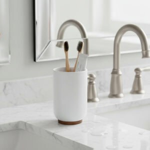 White bathroom tumbler holding toothbrushes on marble sink