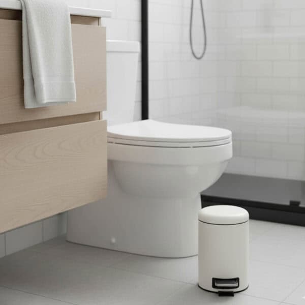 Small white round step trash can on bathroom floor next to toilet and vanity