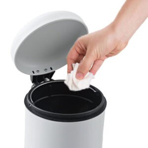Hand disposing tissue into open white step trash can with soft-close lid mechanism visible