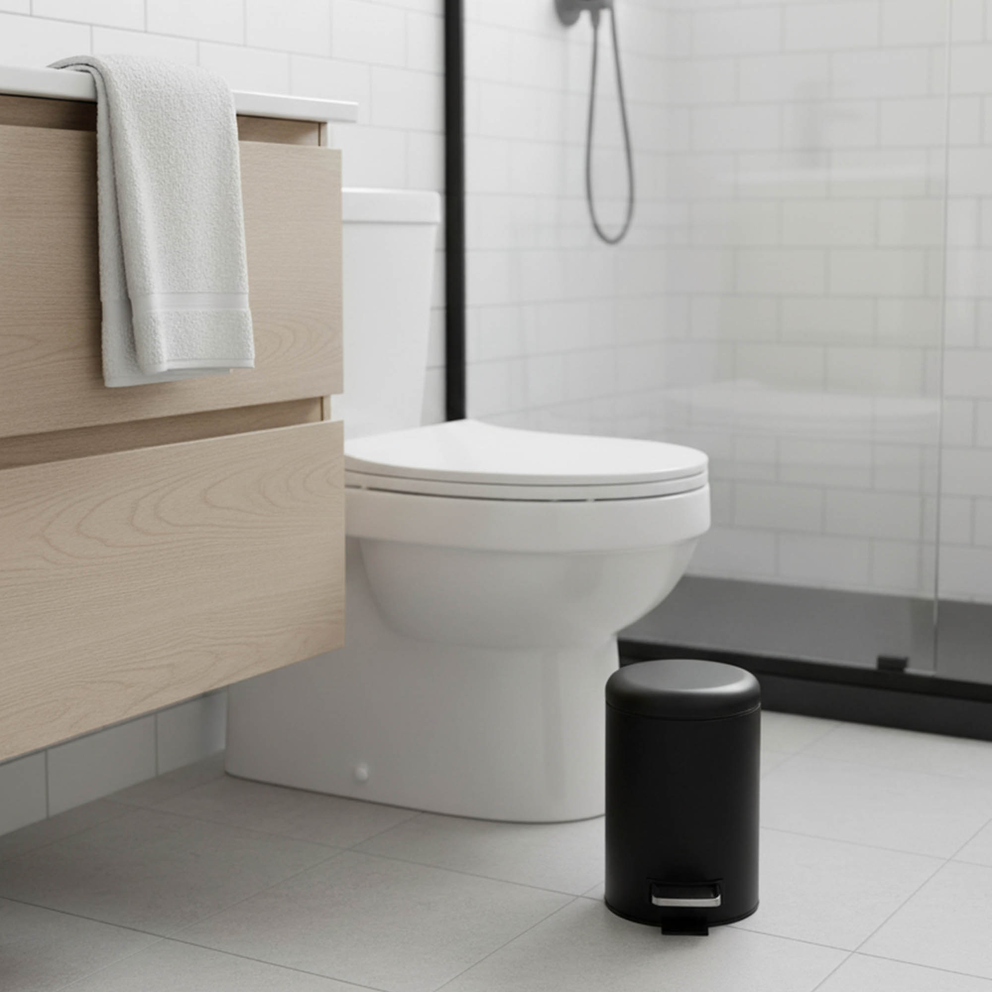 Matte black small bathroom trash can next to toilet with foot pedal