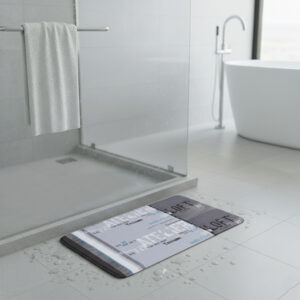 Atelier Loft print bath mat with French text typography in grey tones on wet bathroom floor near glass shower