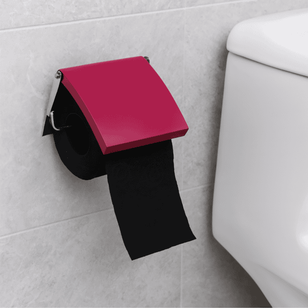 Fuchsia cover toilet paper holder screw-mounted on grey tile beside a toilet tank, holding a black roll under a flip-up fuchsia cover with paper hanging down.