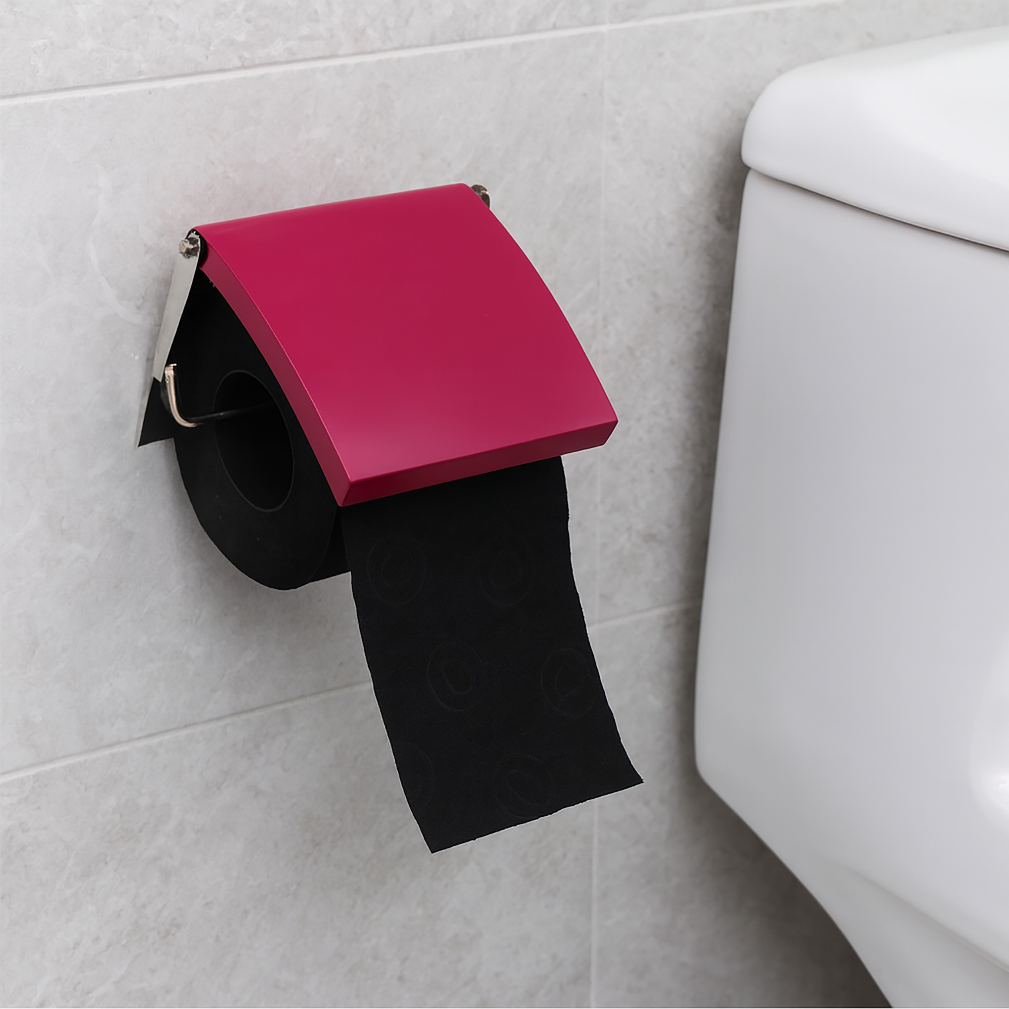 Fuchsia cover toilet paper holder screw-mounted on grey tile beside a toilet tank, holding a black roll under a flip-up fuchsia cover with paper hanging down.