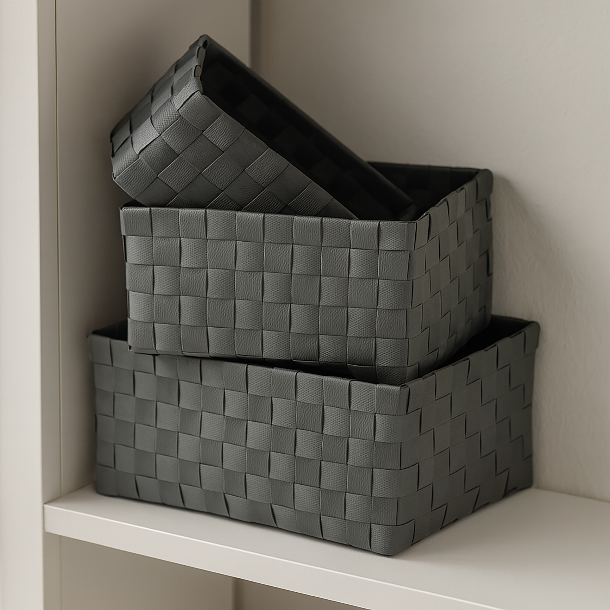 Two gray woven strap baskets stacked on a white shelf, shown empty.
