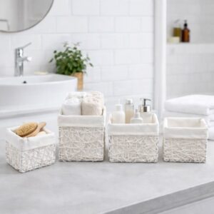 Four white paper rope baskets with linen liners displayed on a bathroom countertop filled with bath brushes, rolled towels, and skincare bottles.