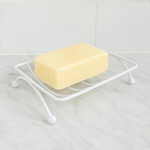White metal wire soap dish with ball feet holding a yellow bar of soap on a marble surface