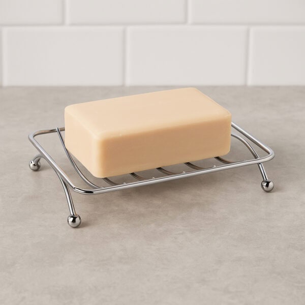 Chrome metal wire soap dish with ball feet holding yellow bar soap on gray counter