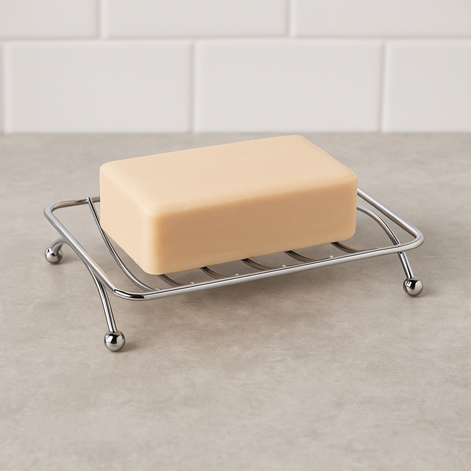 Chrome metal wire soap dish with ball feet holding yellow bar soap on gray counter