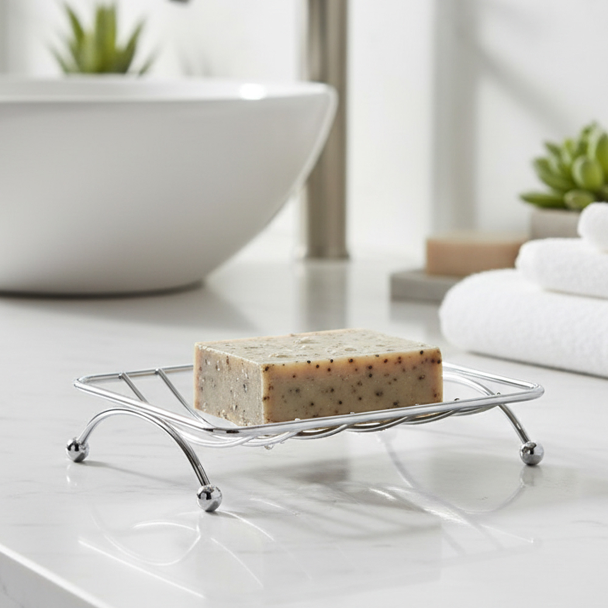 Chrome wire soap holder with speckled bar soap on white bathroom counter near sink