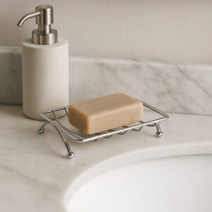 Chrome wire soap dish with beige bar soap next to soap dispenser on marble counter