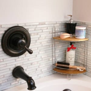 Image 6: Chrome 2-shelf corner storage tower with bamboo shelves holding bath products and a brush in a tiled shower corner beside a faucet.