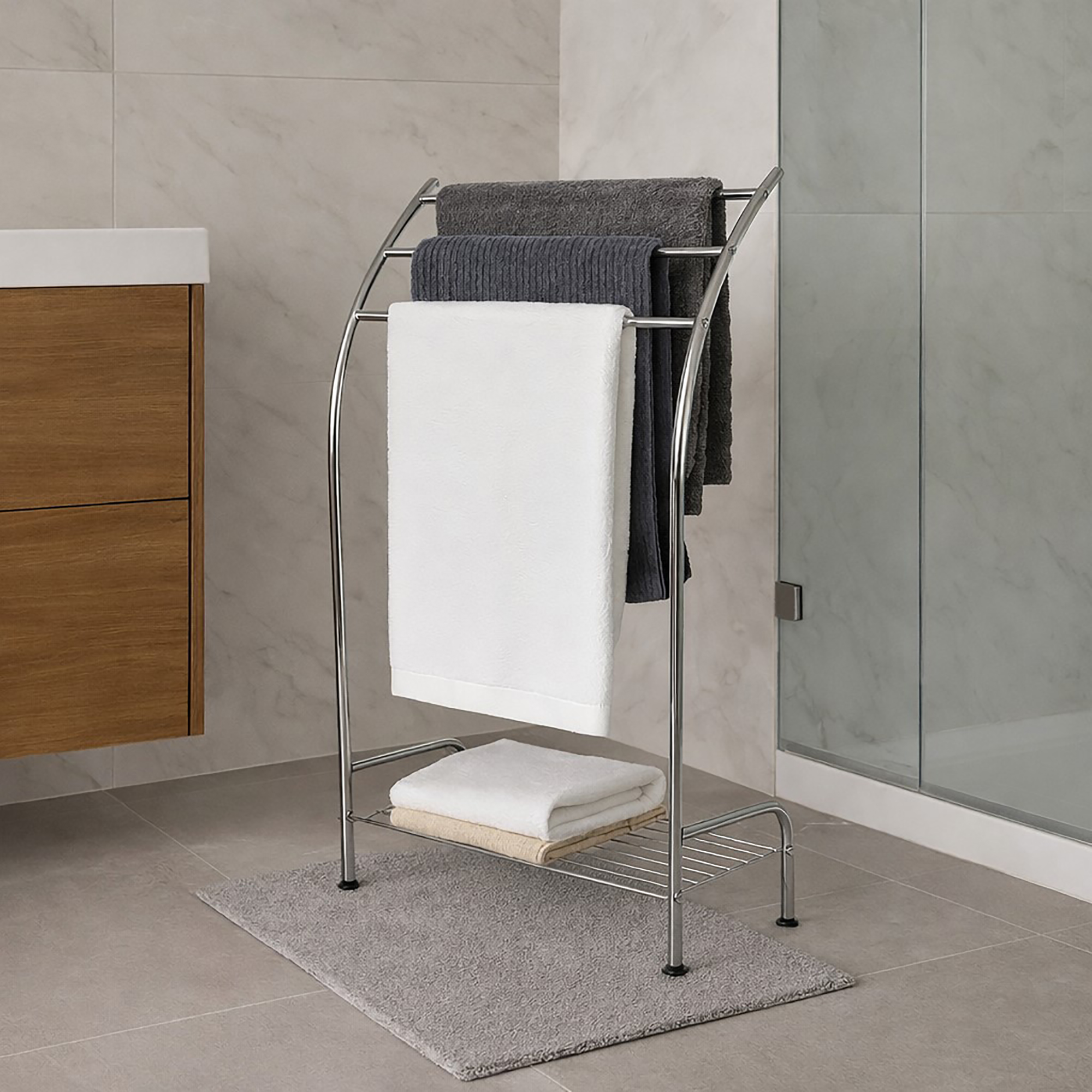 "Chrome 3-bar towel rack holding gray and white towels with folded towels on bottom shelf, next to glass shower"