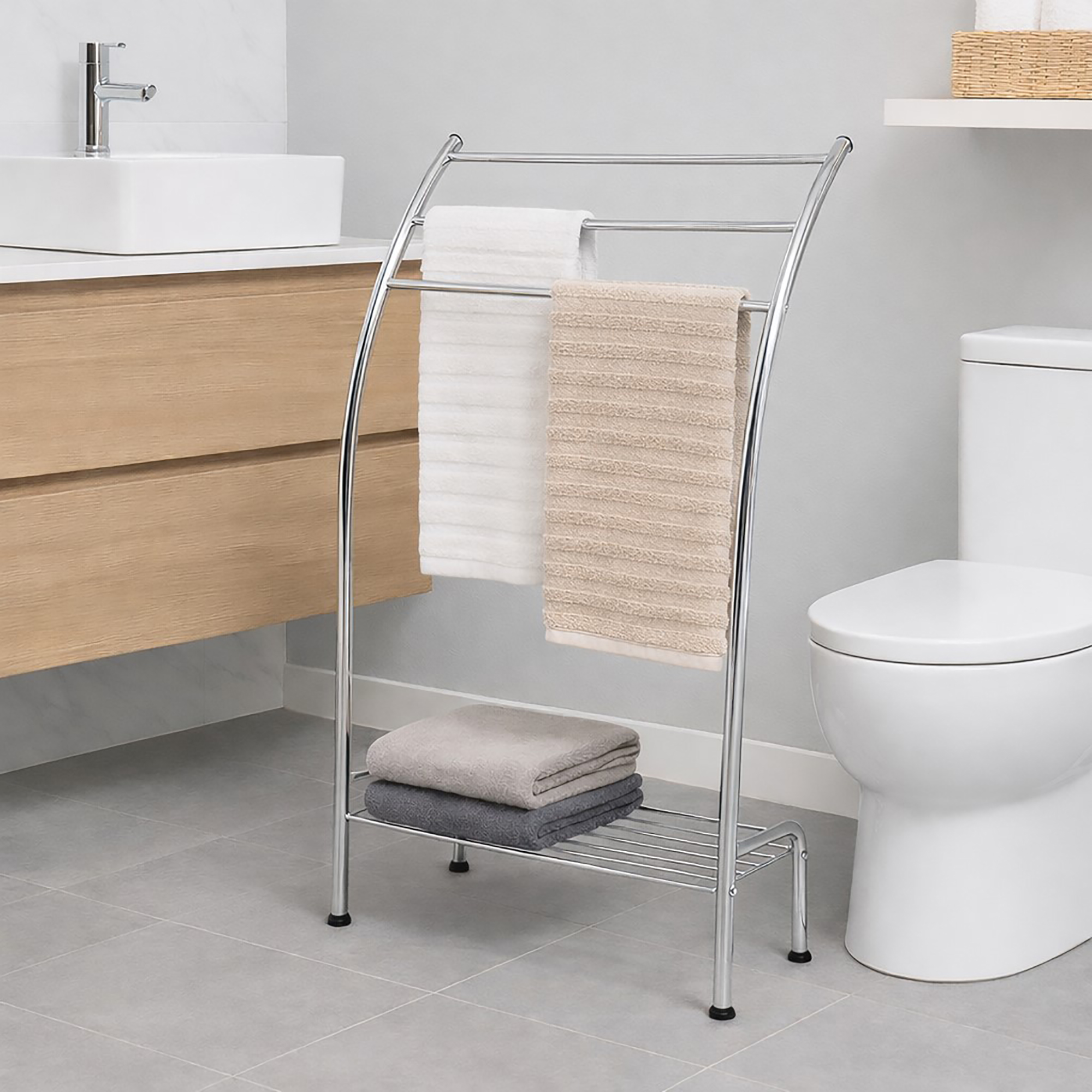 "Chrome curved towel rack holding white and beige towels with folded towels on bottom shelf, next to toilet"