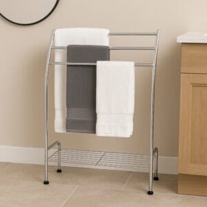 "Chrome curved freestanding 3-bar towel rack with bottom shelf holding gray and white towels in beige bathroom"