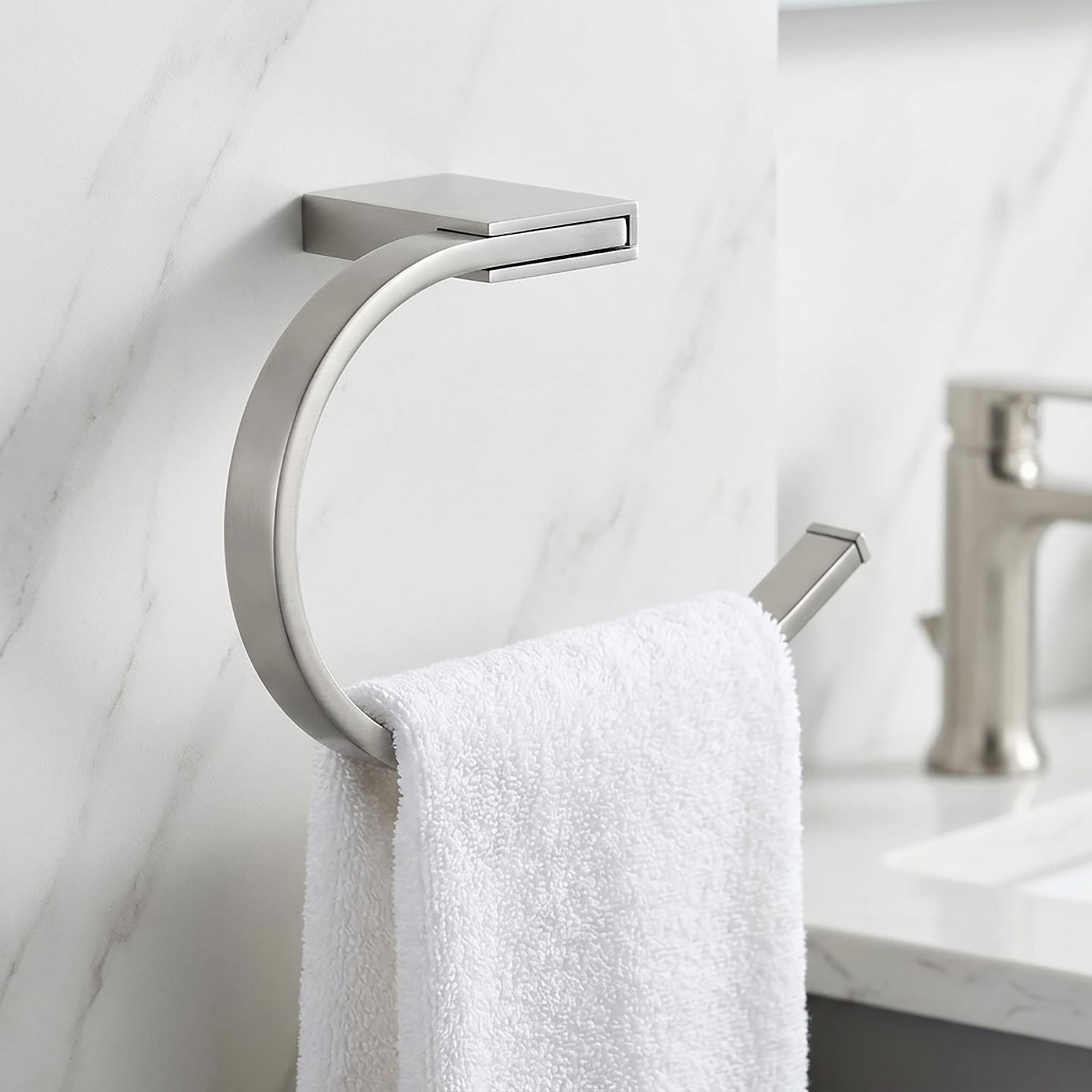 "Brushed nickel open towel ring with white towel on marble wall near sink"