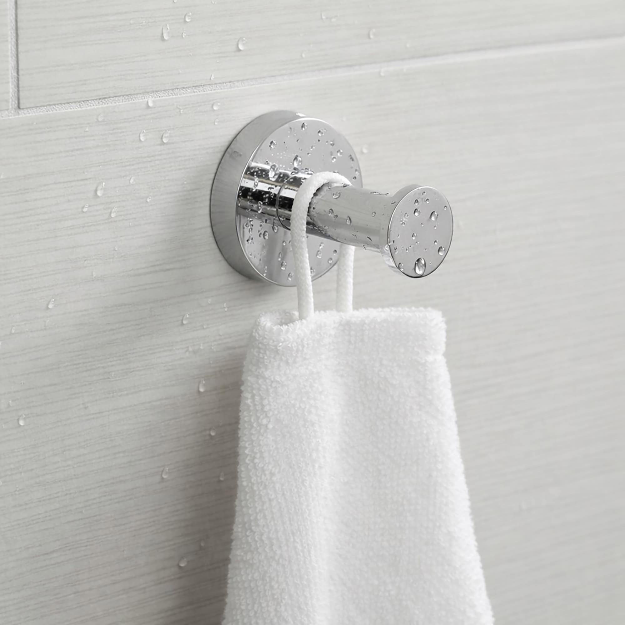 "Chrome robe hook with white towel hanging on wet gray tile wall"