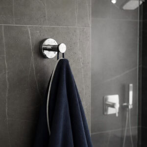 "Chrome robe hook with navy towel on wet dark stone tile wall near shower"