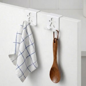"Two white figure hooks on white cabinet holding blue plaid dish towel and wooden spoon"
