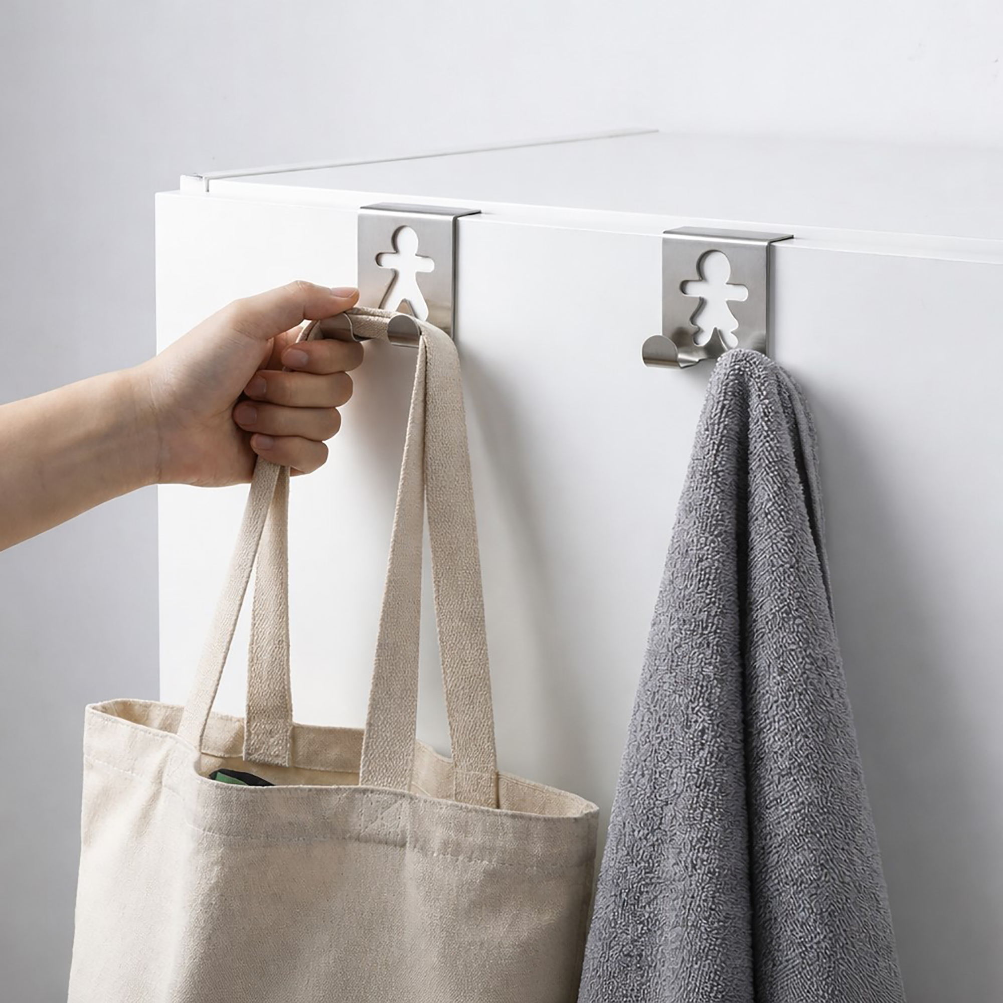 "Hand removing tote bag from stainless steel figure-shaped cabinet hook beside second hook holding gray towel"