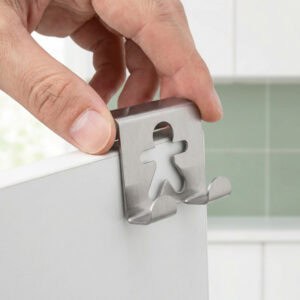 "Close-up of hand placing brushed steel gingerbread figure hook over white cabinet edge"