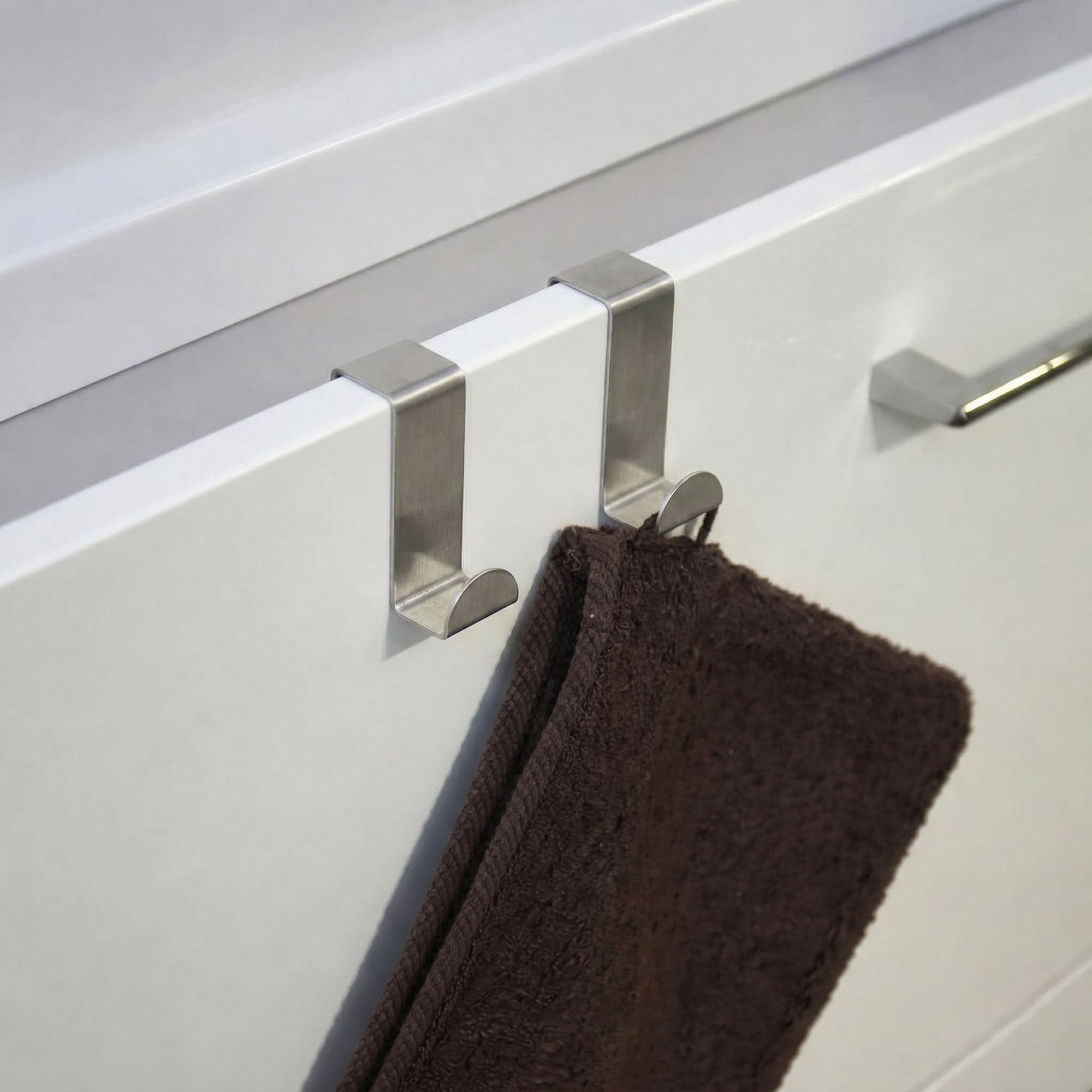 "Two stainless steel hooks on white cabinet door holding a brown towel"