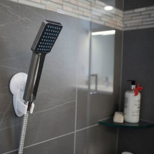 "Square chrome handheld shower head in white suction bracket on dark gray tile"